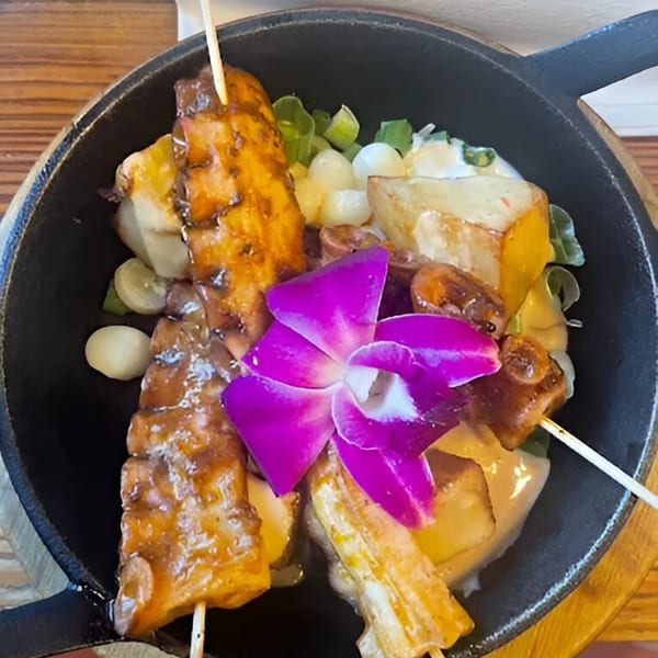 Peruvian anticuchos with a purple orchid garnish, served in a black skillet.