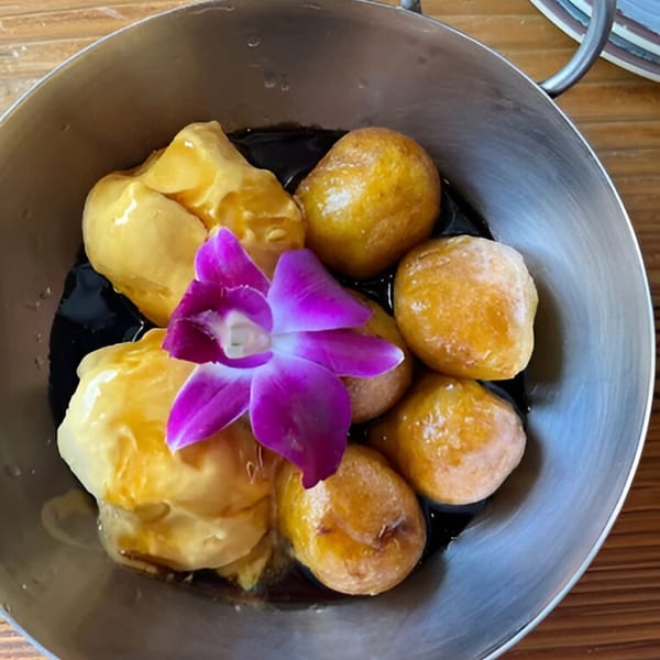 Peruvian picarones, golden fried doughnuts, with a purple orchid in a metal bowl.