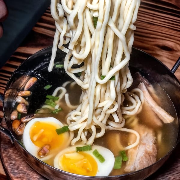 Peruvian ramen with thick noodles, soft-boiled eggs, corn, and meat in a rich broth.