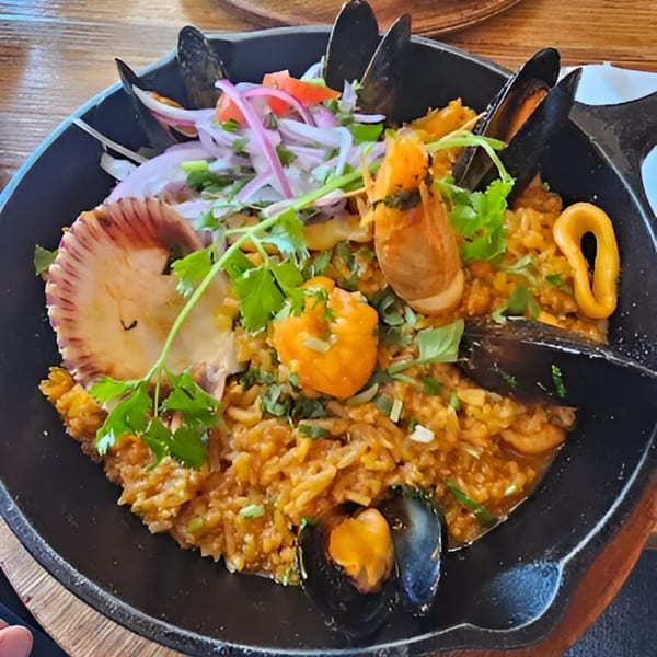 Peruvian seafood paella with mussels, scallops, shrimp, and calamari, garnished with red onion and cilantro.