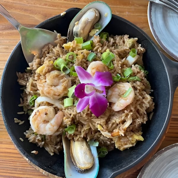 Peruvian chaufa de mariscos with shrimp, mussels, and a purple orchid in a black skillet.