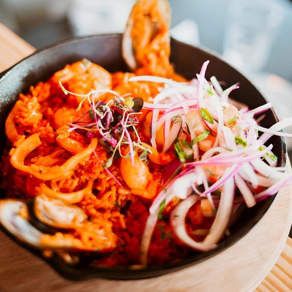 Peruvian Arroz con Mariscos, a seafood rice dish, garnished with red onions and microgreens.