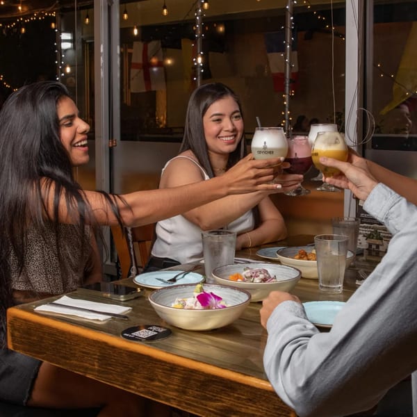Three people toasting Peruvian Pisco Sours and eating ceviche at Ceviches by Divino.