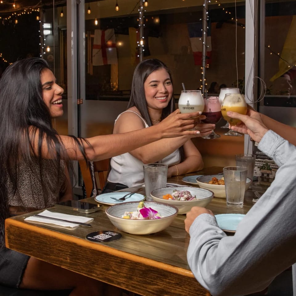 Three people toasting Peruvian Pisco Sours and eating ceviche at Ceviches by Divino.
