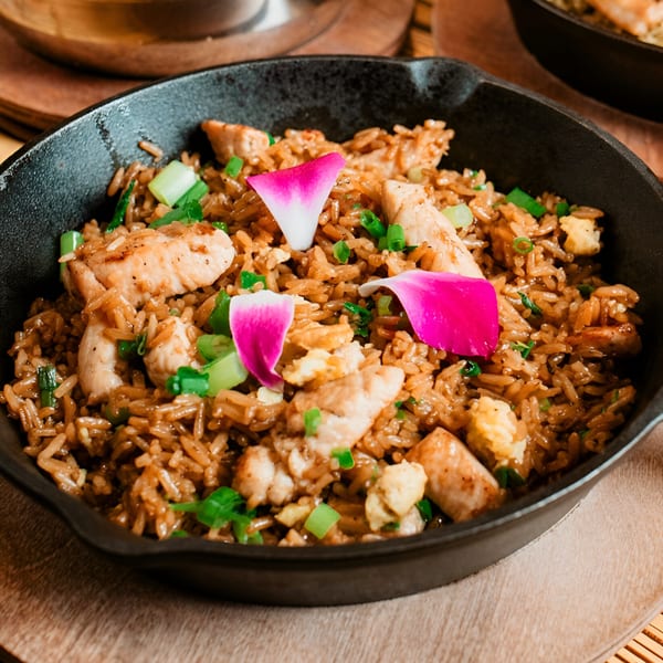 Peruvian fried rice with chicken, green onions, and pink flower petals in a black skillet.