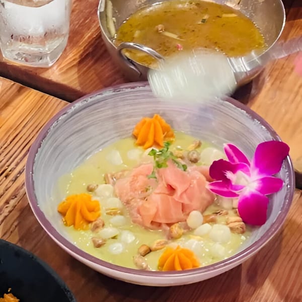 Peruvian ceviche with pink fish, orange puree, white corn, and a purple orchid garnish.
