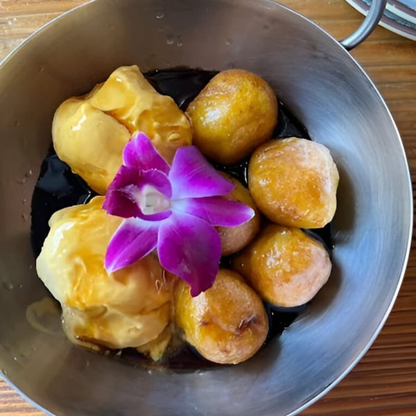 Peruvian picarones, golden doughnuts with syrup and a purple orchid, in a metal bowl.