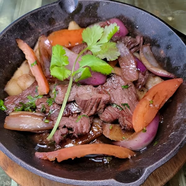 Peruvian Lomo Saltado in a cast iron skillet, featuring beef, onions, tomatoes, and cilantro.