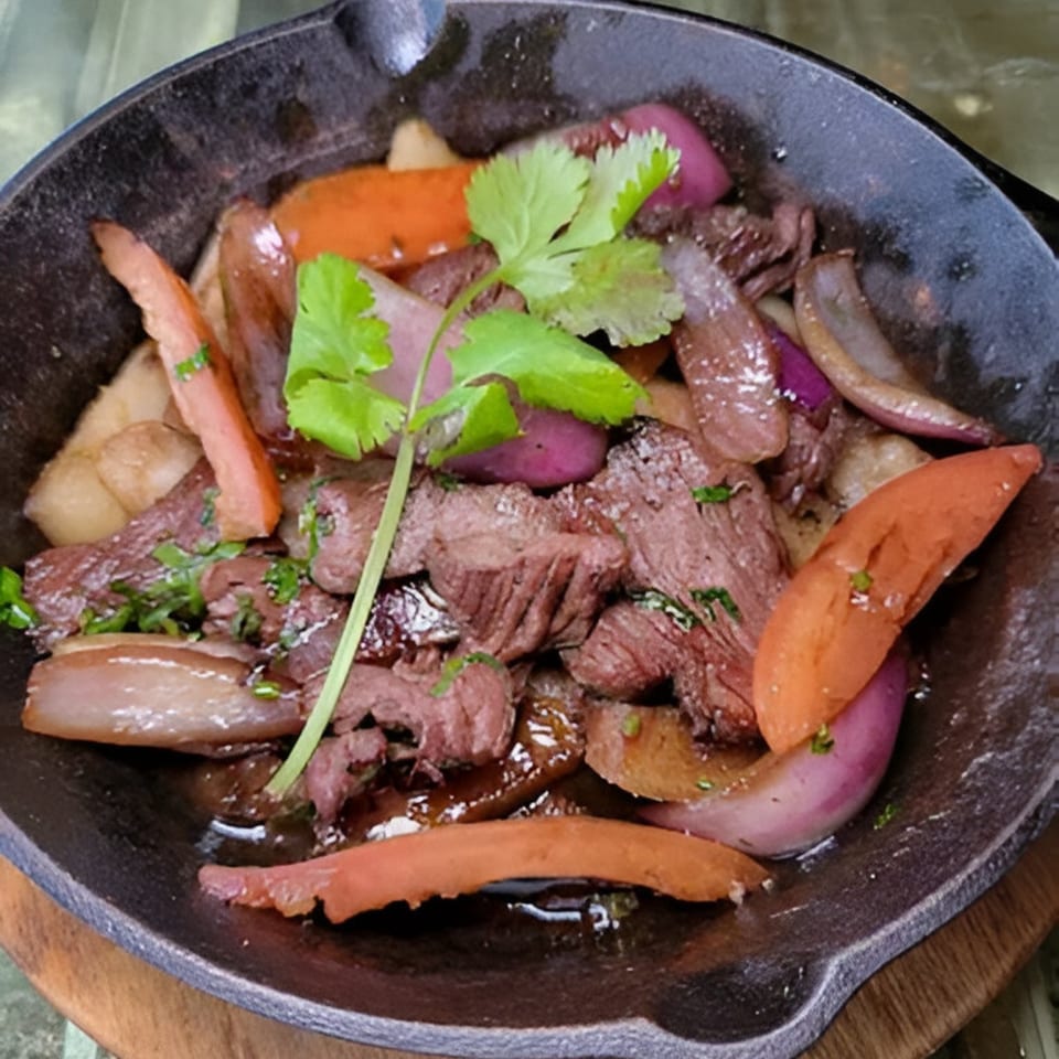 Peruvian Lomo Saltado in a cast iron skillet, featuring beef, onions, tomatoes, and cilantro.