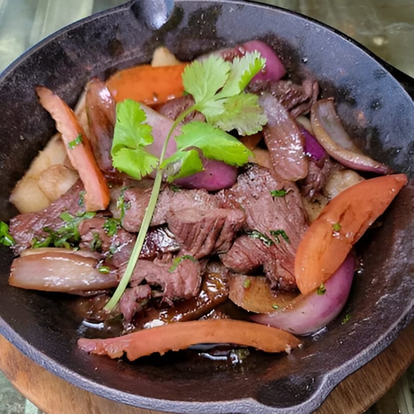 Peruvian Lomo Saltado in a cast iron skillet, featuring beef, onions, tomatoes, and cilantro.