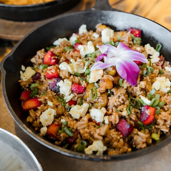 Peruvian fried rice with strawberries, scrambled egg, green onions, and a purple orchid in a skillet.