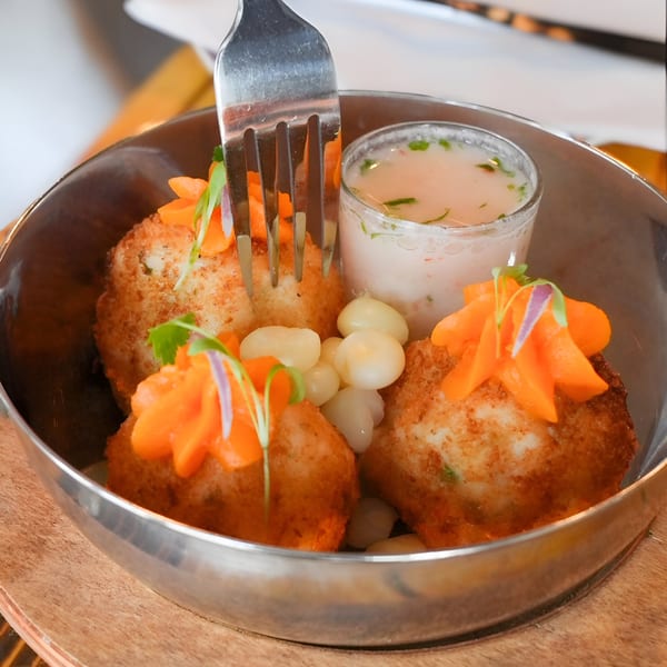 Peruvian fried seafood cakes with carrots, corn, and a creamy sauce in a metal bowl.