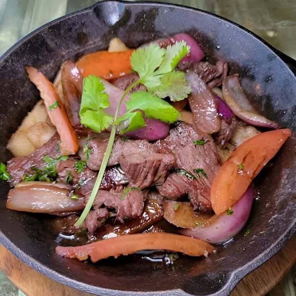 Peruvian Lomo Saltado with beef, red onions, tomatoes, and cilantro in a cast iron pan.
