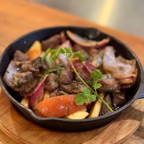 Peruvian Lomo Saltado with beef, red onions, tomatoes, and french fries in a cast iron skillet.