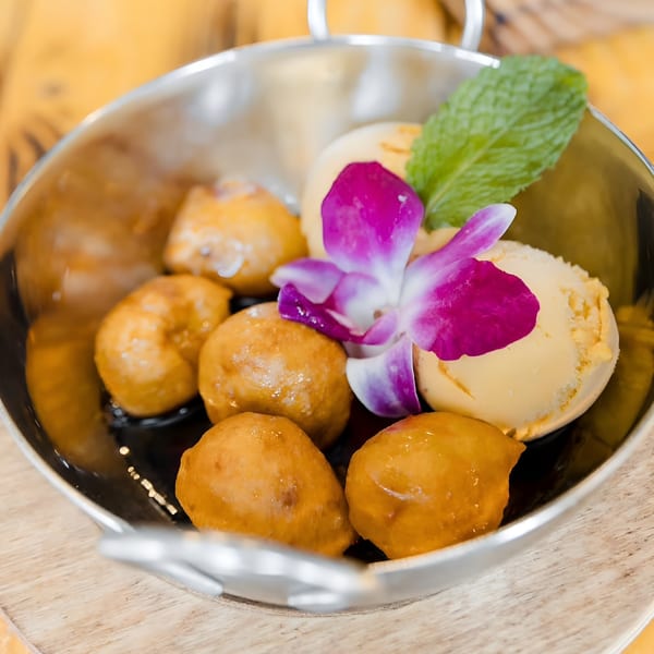 Peruvian picarones with ice cream, garnished with a purple orchid and mint, in a metal bowl.
