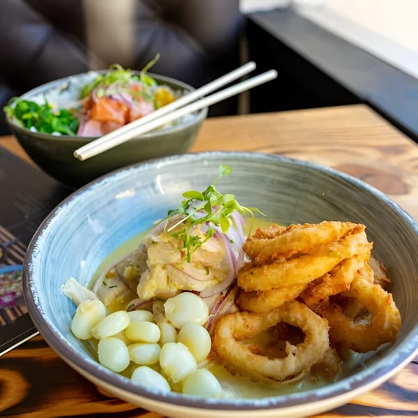 Peruvian ceviche with fried calamari and corn, with a poke bowl in the background.